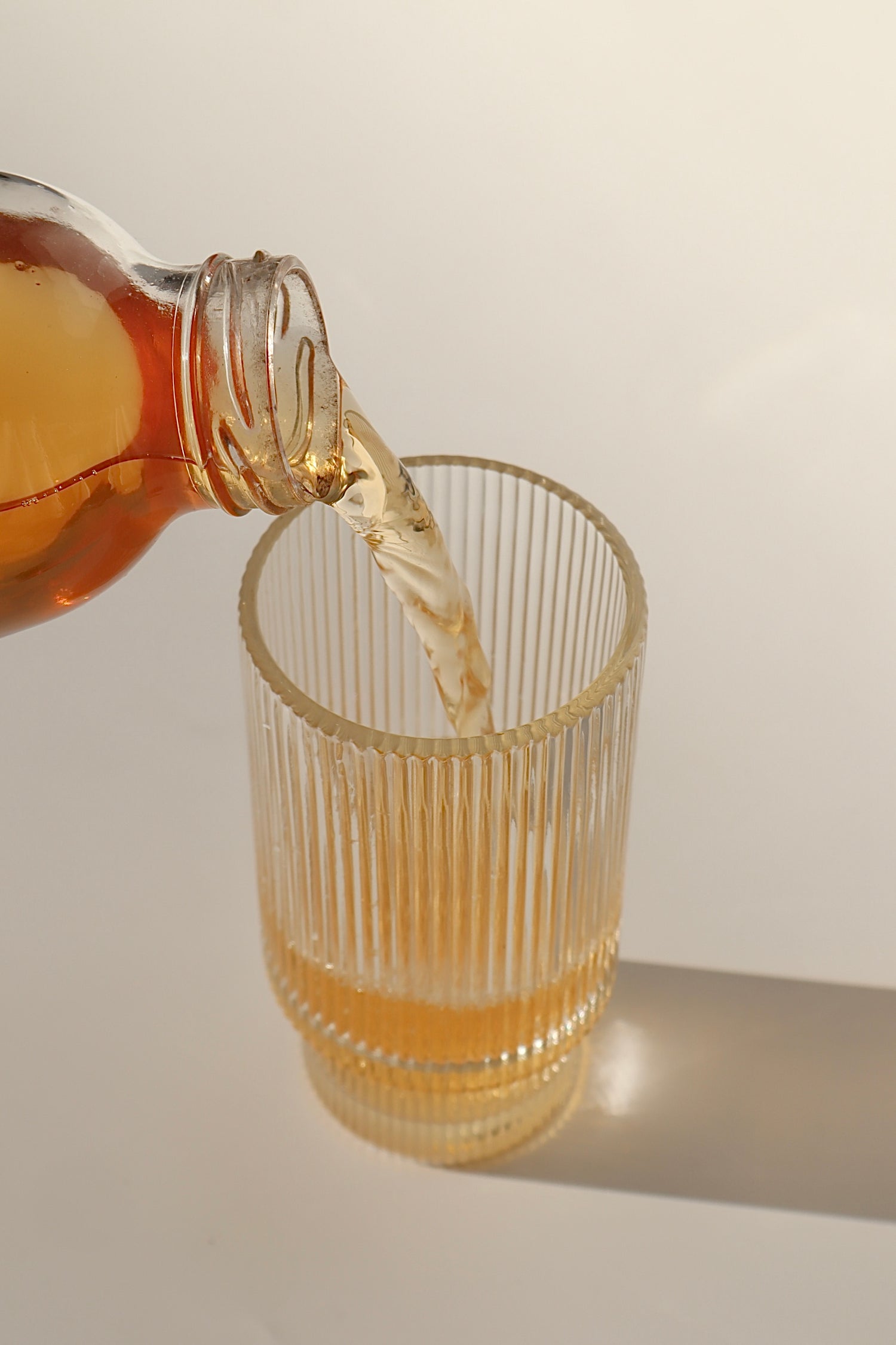 Photo of a delicious, fresh, raw and totally natural glass of kombucha being poured into a fancy glass, against an aesthetic background with nice shadows being cast - boochacha
