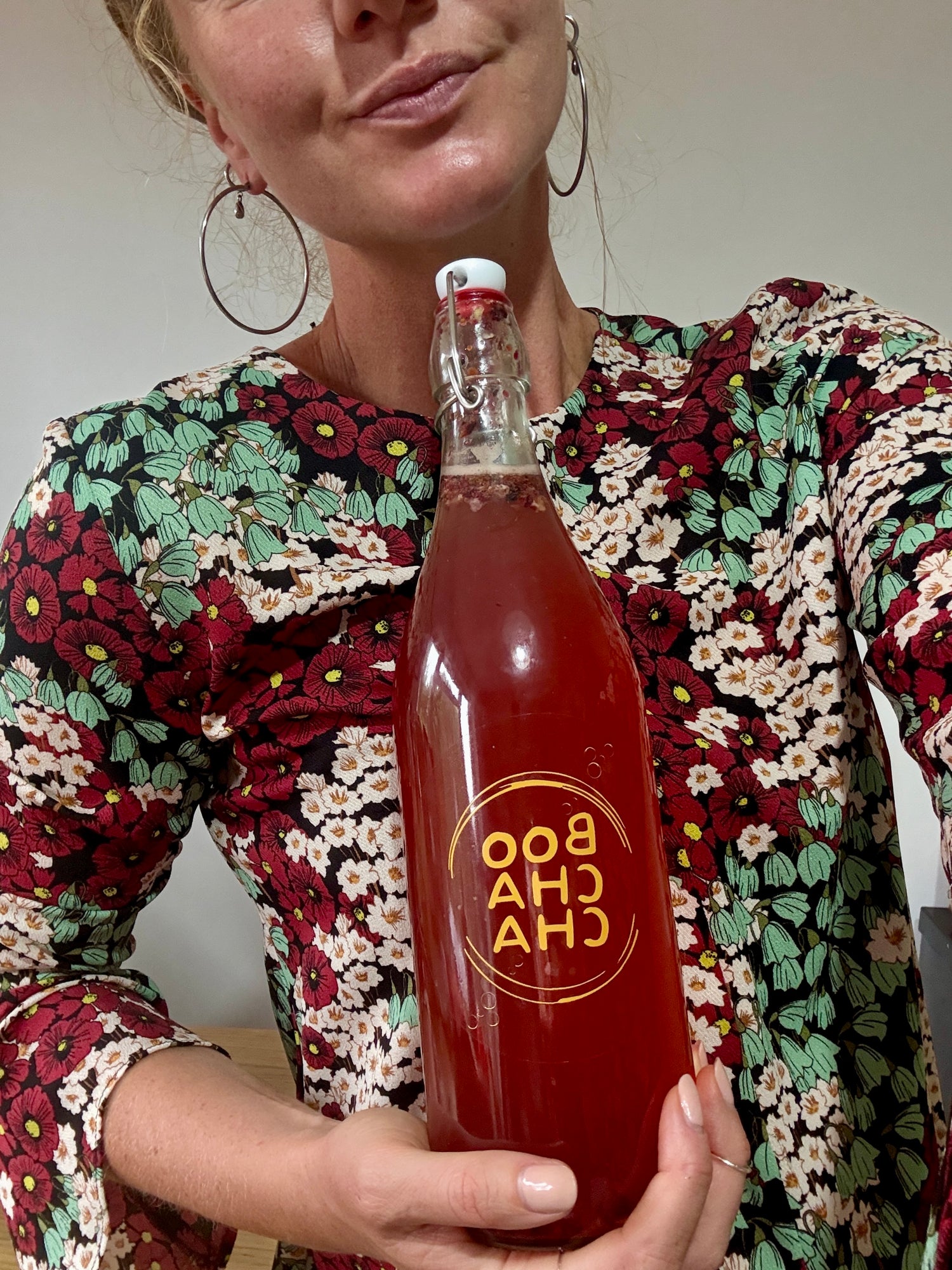 Person holding bottle of homemade Kombucha boochacha looking proud, in coordinating outfit.