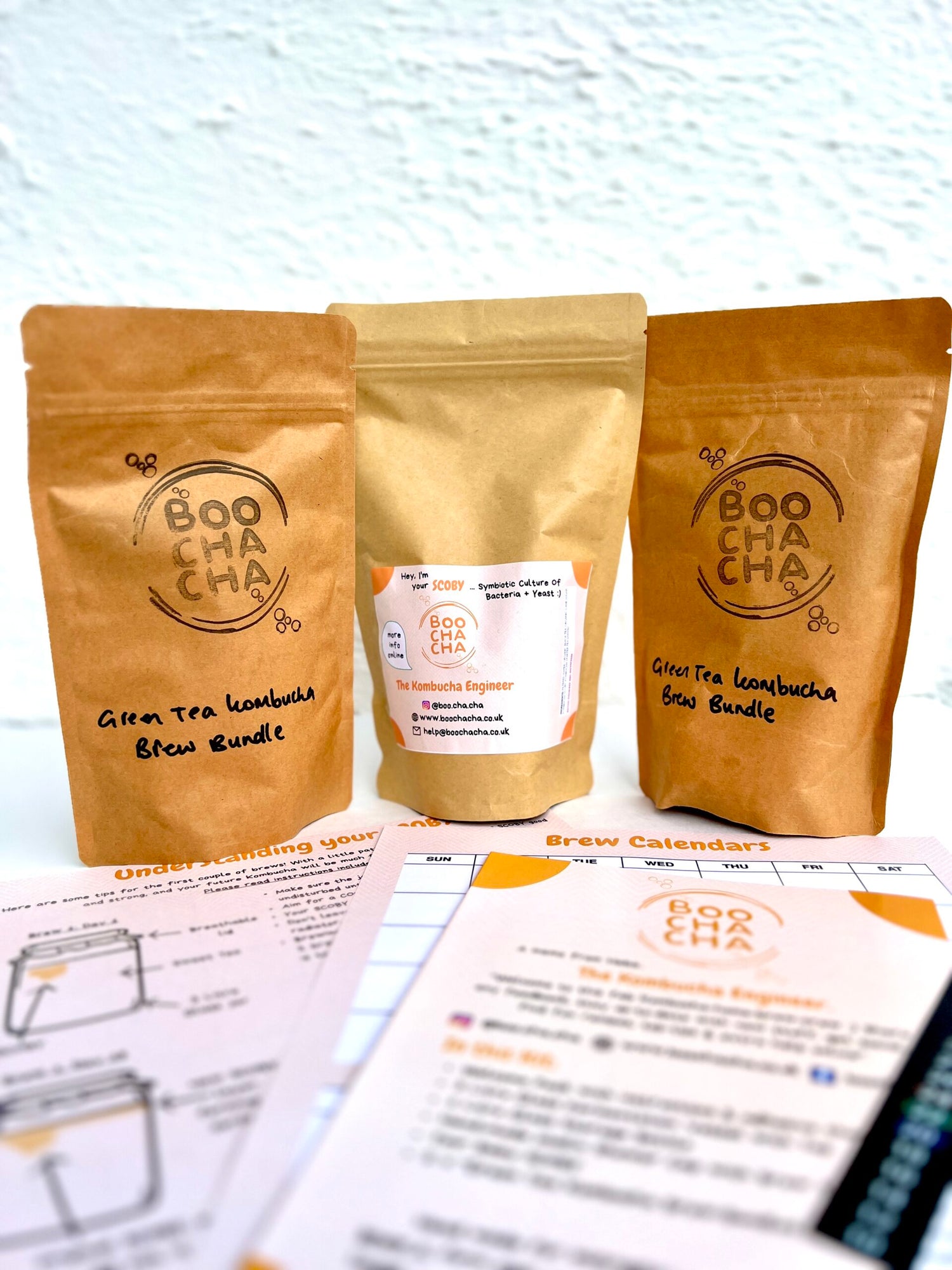 Professional photo of basic kombucha starter kit, with fun style instructions on display, branding bright and vibrant, sustainable packaging, brew bundles and baby scoby in eco packaging - boochacha