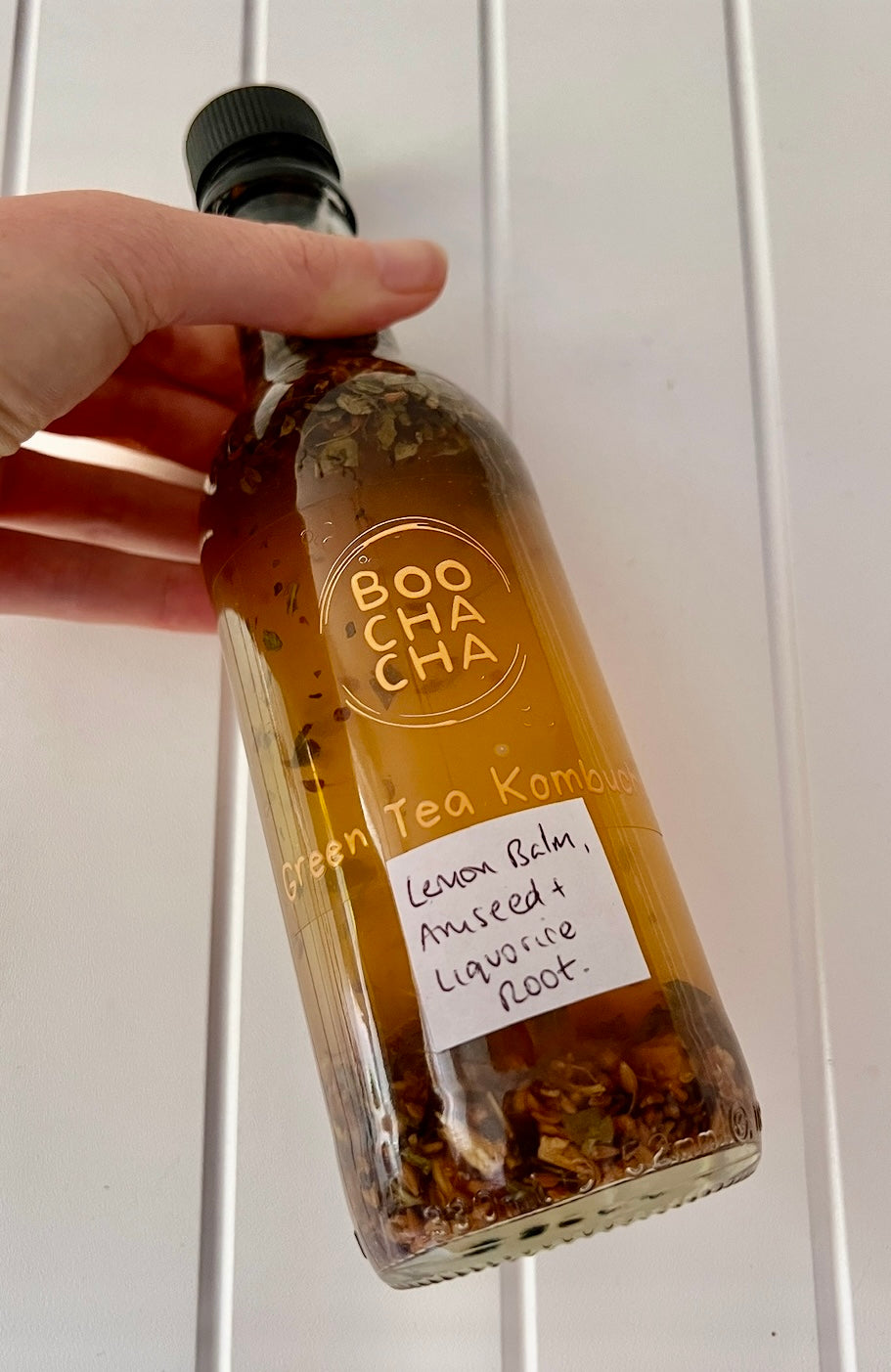 Bottle labeled 'BOO CHA CHA' with a hand holding it against a white background.