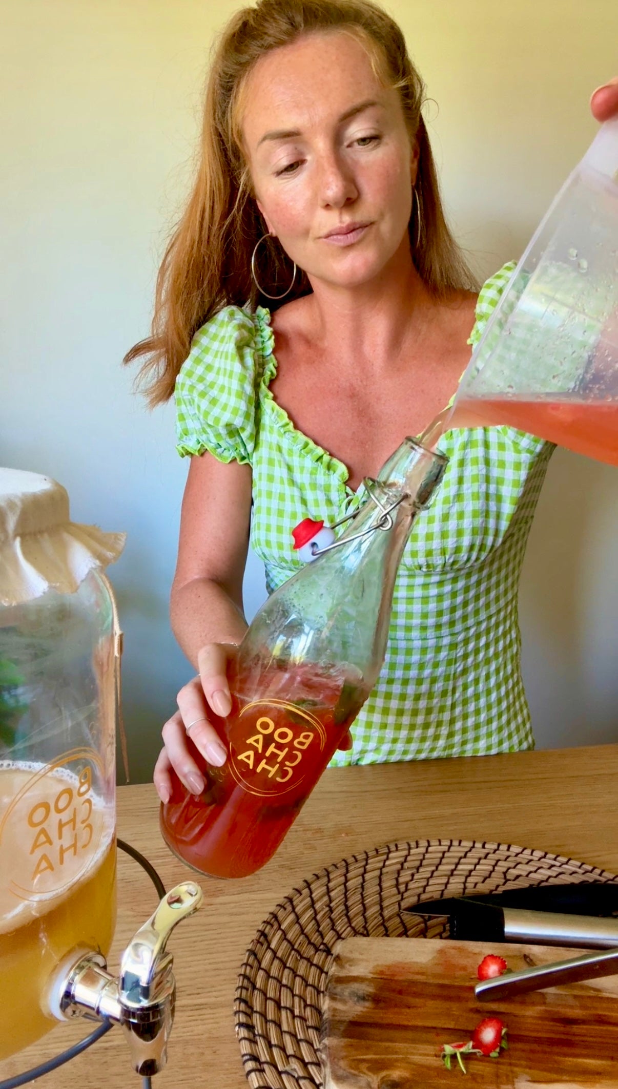 Woman pouring a drink from a bottle into a glass on a wooden table.